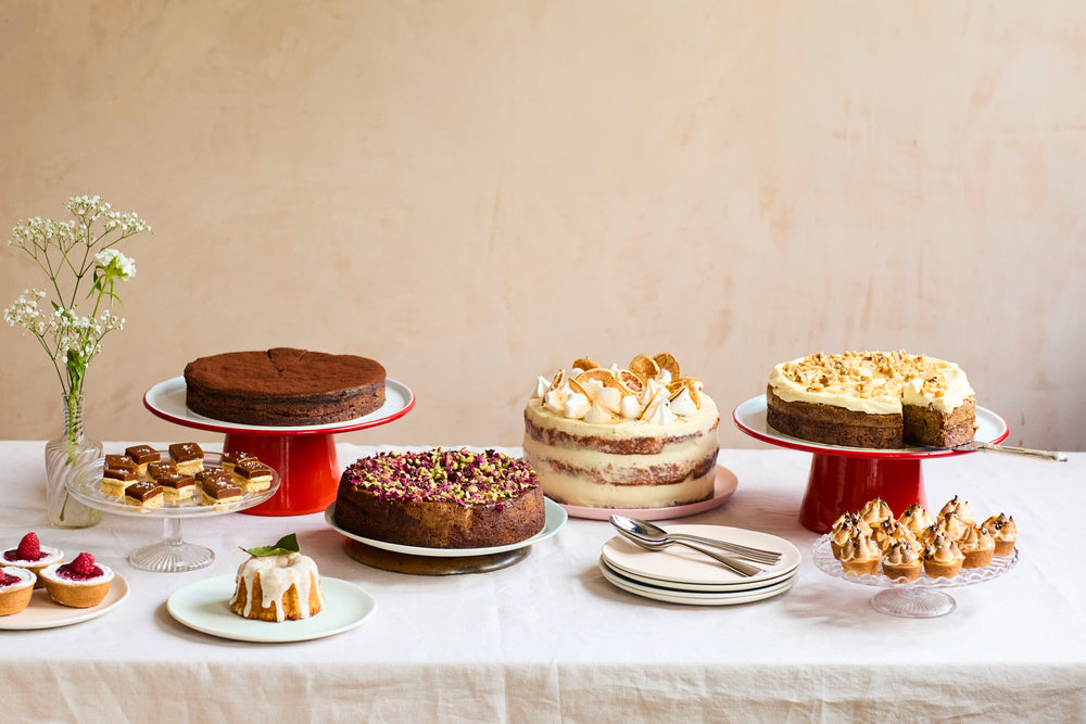 A display of cakes: cheesecake tarts, caramel tahini shortbreads, Sicilian lemon teacake, chocolate and rum fondant cake, semolina and rosewater cake, lemon and mascarpone cake, carrot and walnut cake and mini passion fruit meringue tarts