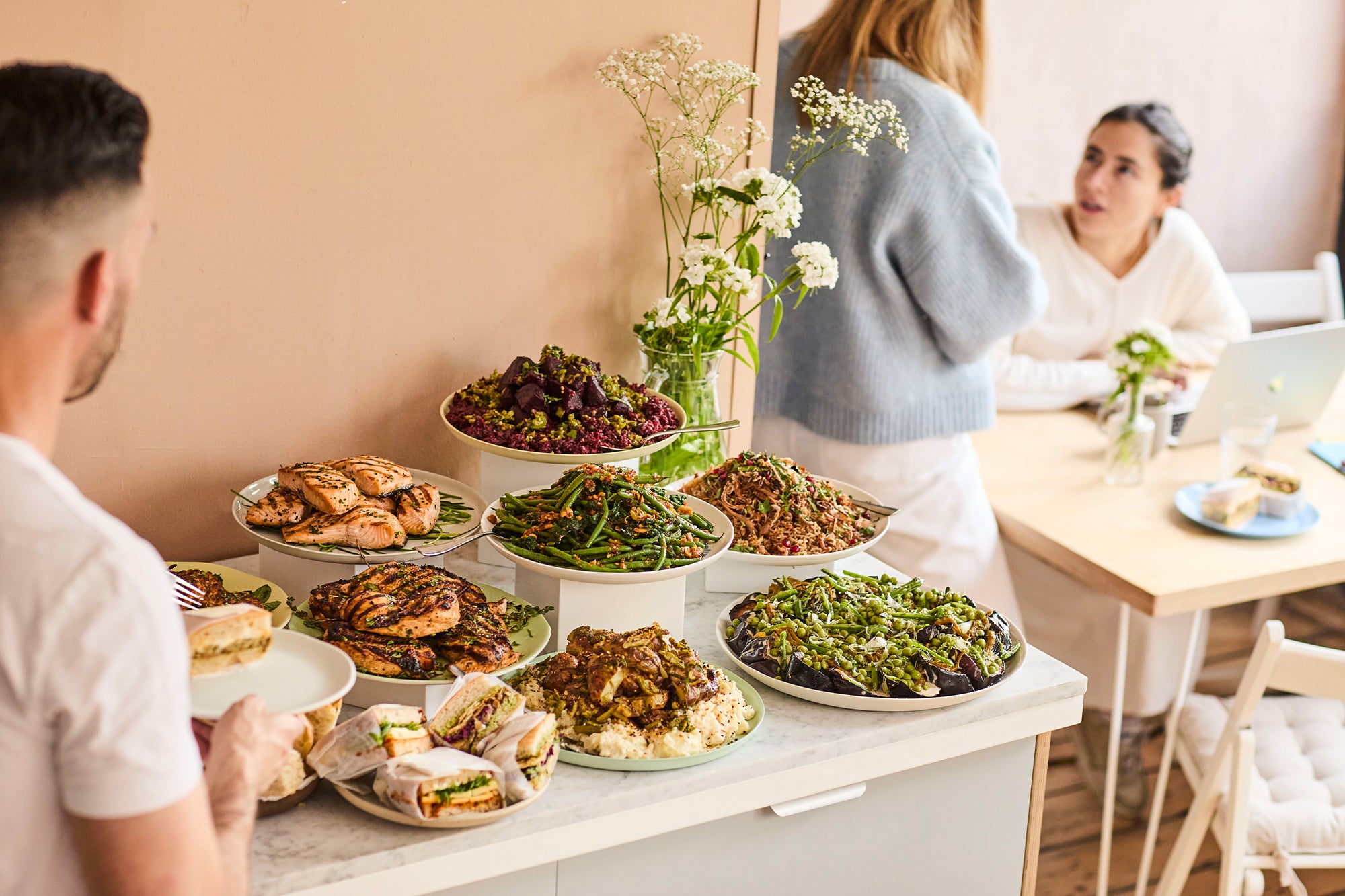 A display with platters of sandwiches, chicken, salmon and salads: potato and cornichon, green beans, beetroot, aubergine and rice