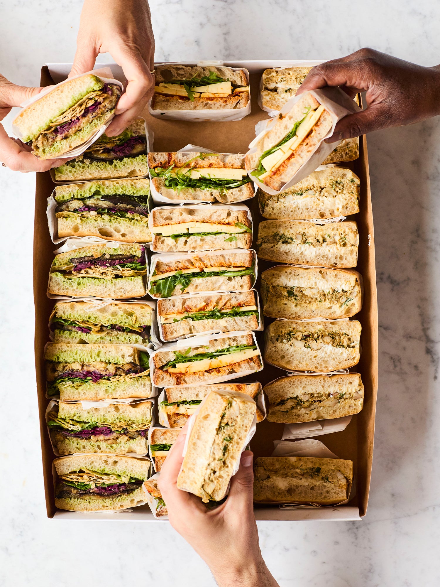 a box filled with sandwiches: cheddar and pickle, aubergine and green tahini, chicken shawarma.