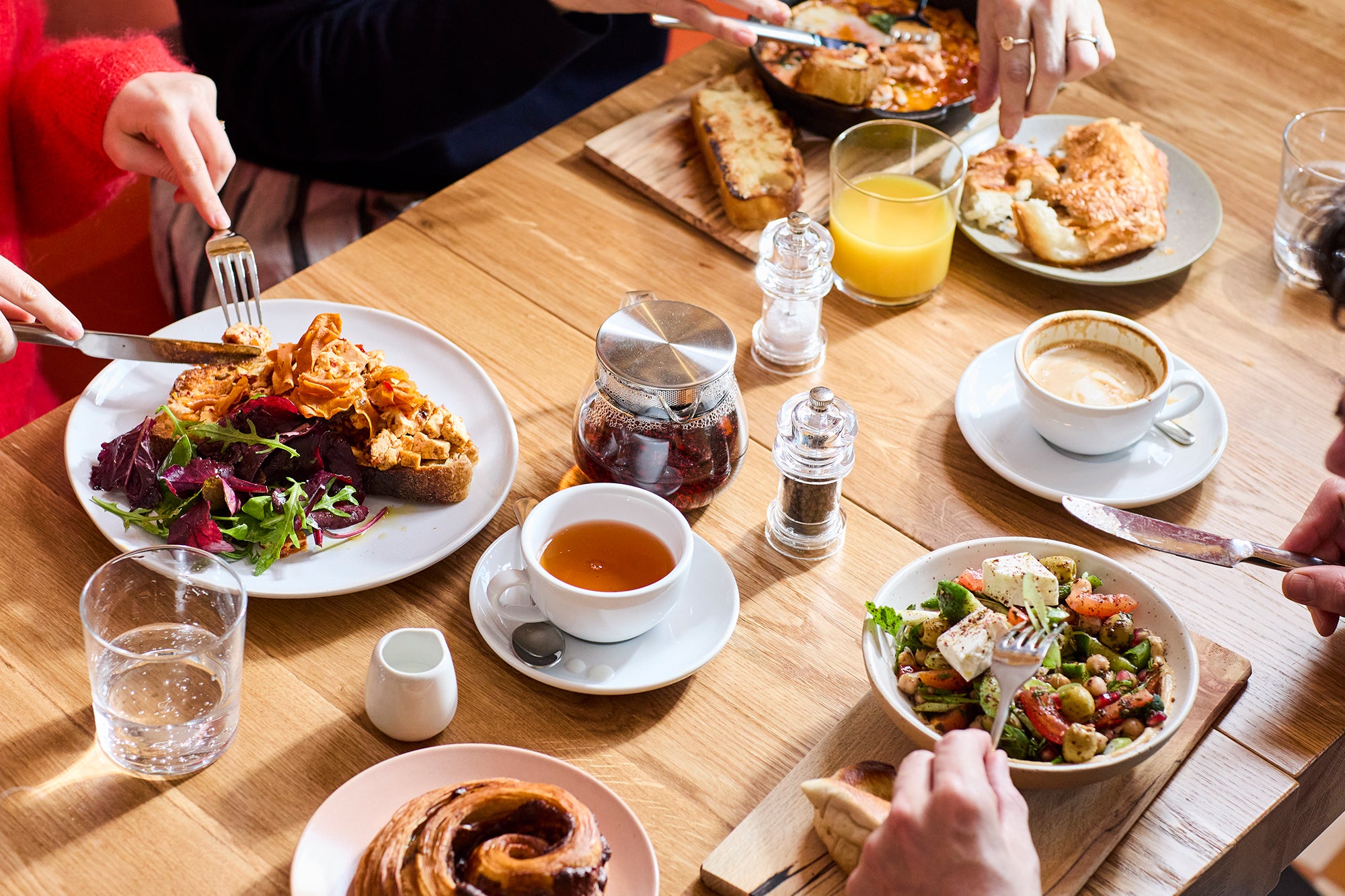 Three people eating breakfast: scrambled eggs, shakshuka, halva Danish and Middle Eastern breakfast. 
