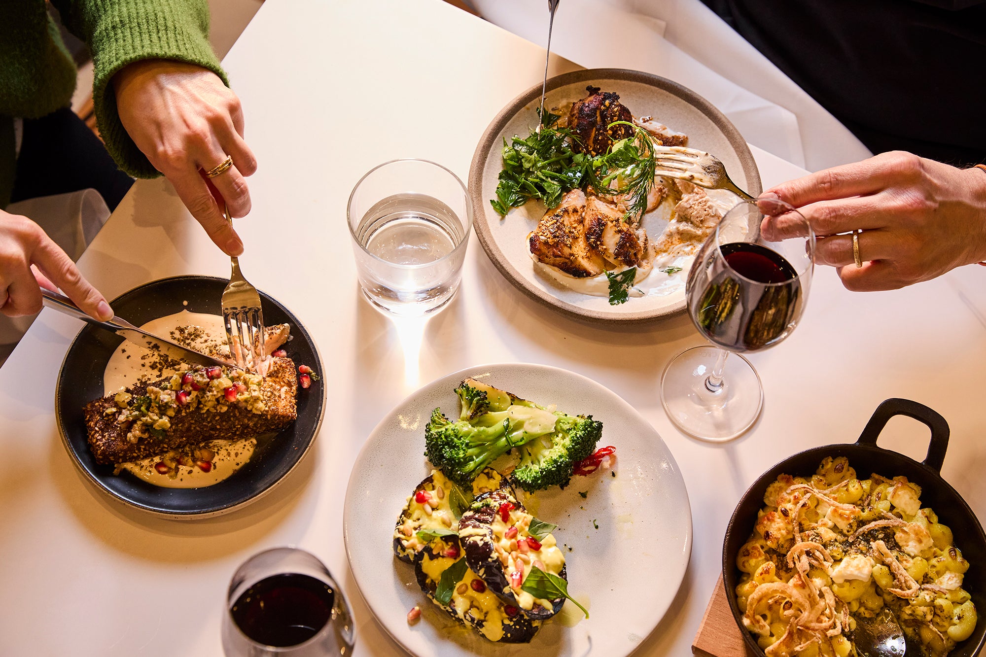 Top view of the dining table with aubergine, salmon, chicken, pasta and broccoli shared by two people.