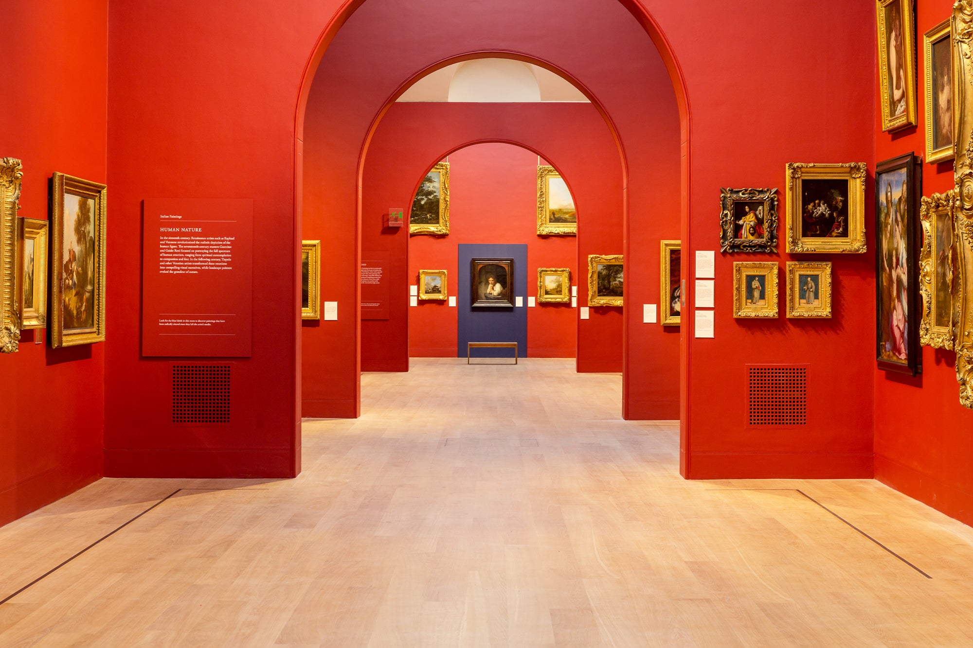 An interior of Dulwich Picture Gallery with red walls and baroque and classical paintings on the walls. 