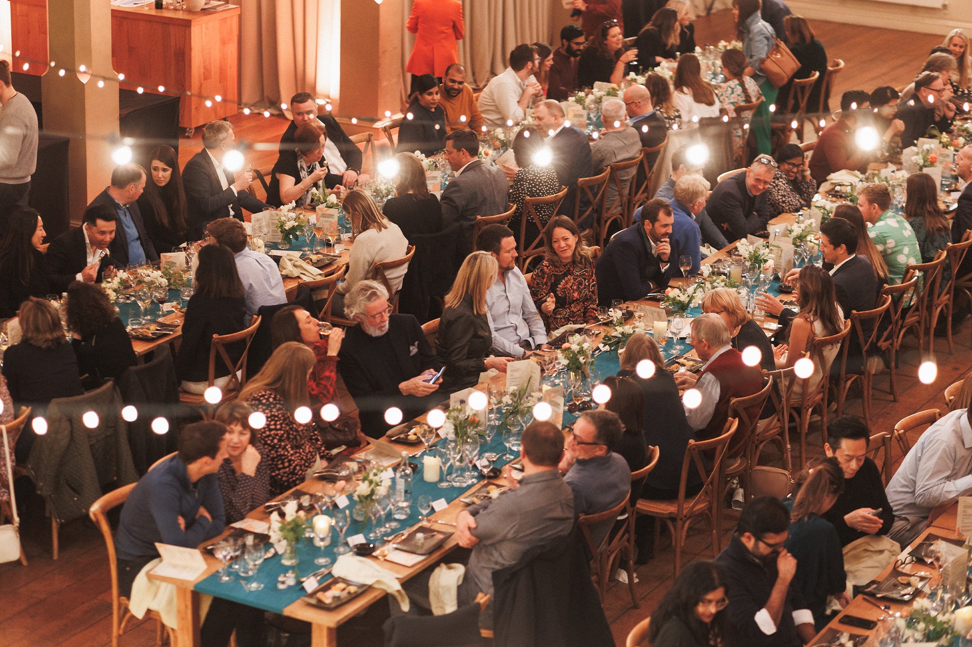 Rows of long dining tables, with guests eating a meal.