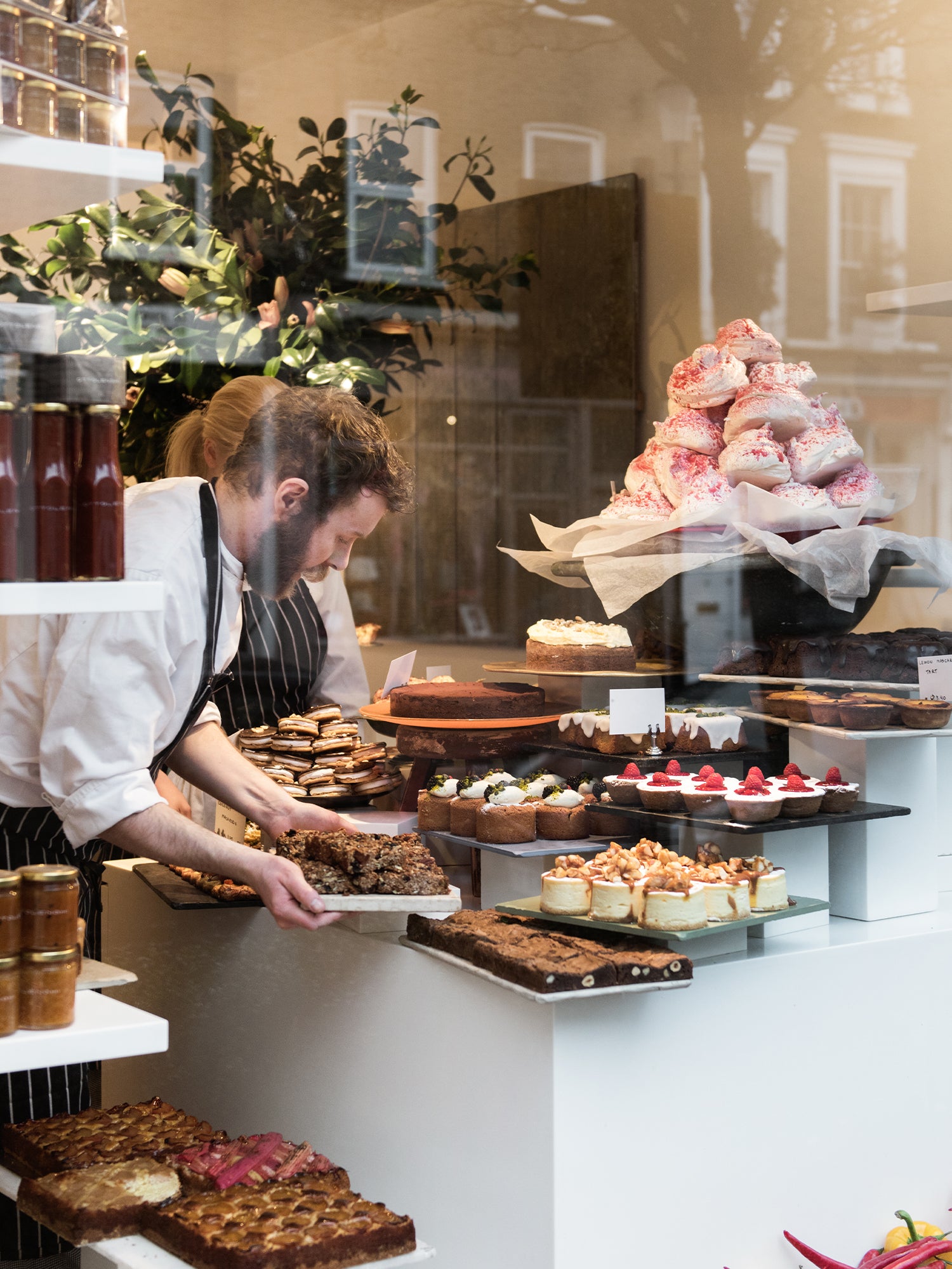Pastry chefs making the display ready for service. Large variety of cakes: cheesecakes, financiers, brownies, meringues , tarts etc. etc.