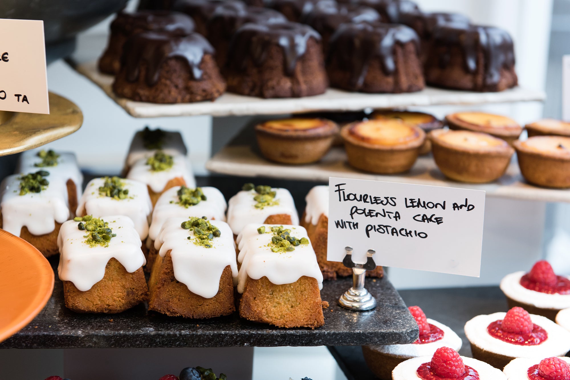 Close up of dessert display with flourless lemon polenta cakes in the foreground; chocolate cakes and lemon tarts at the background