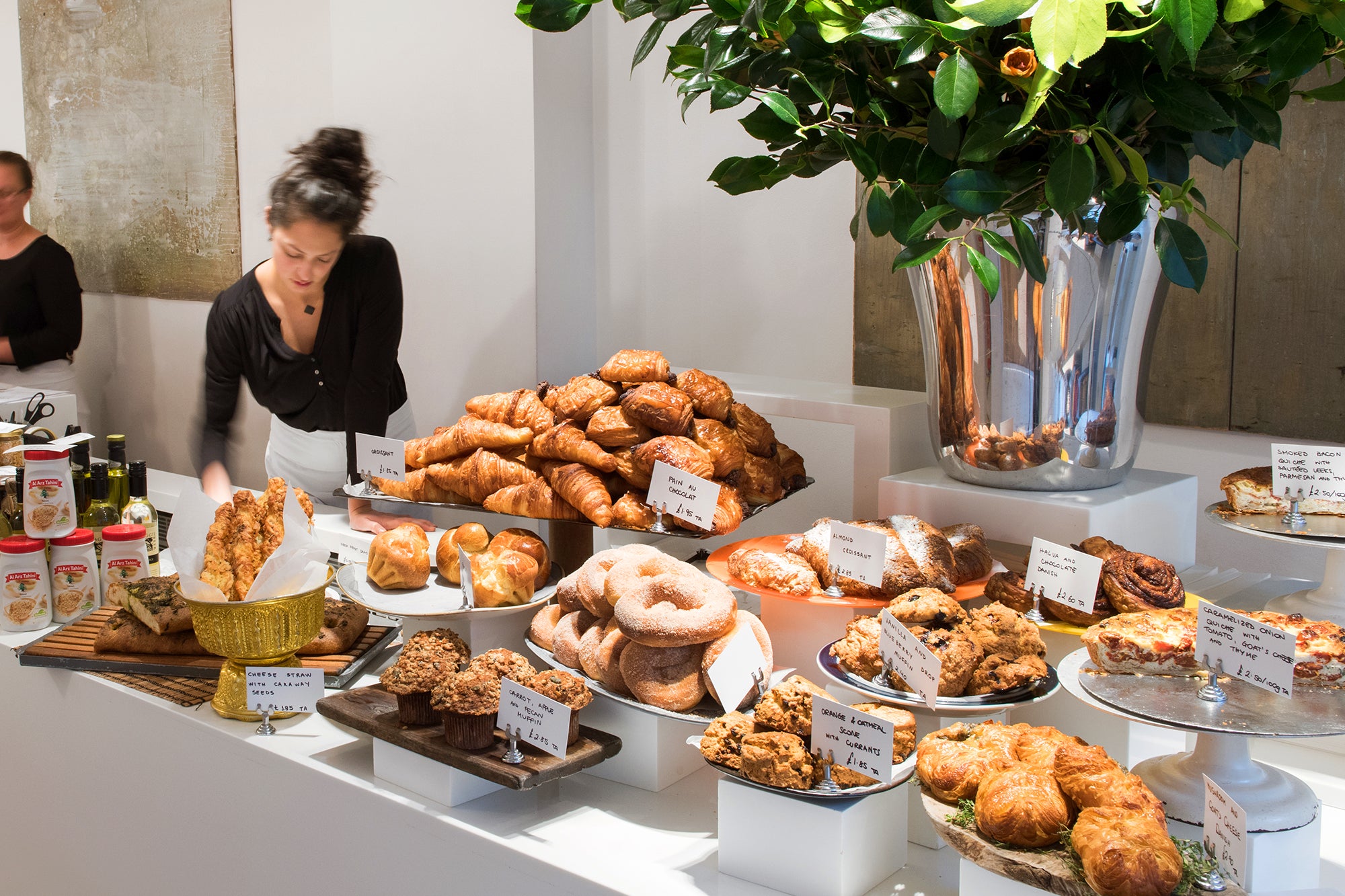 Morning pastry display: with croissants, scones, muffins, Danishes etc. A member of staff preparing display