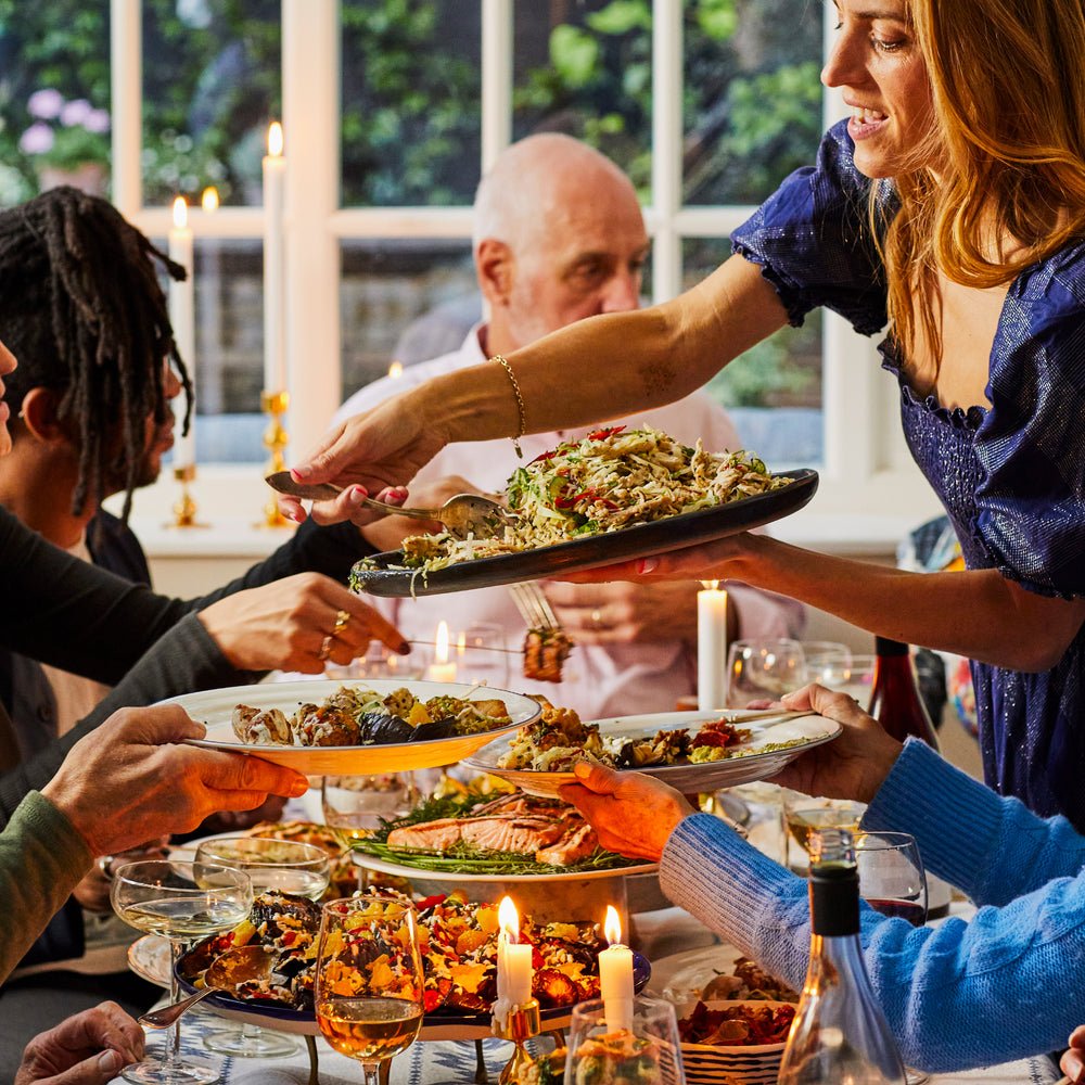 A dinner table with salad and salmon platters with people sharing the food. 