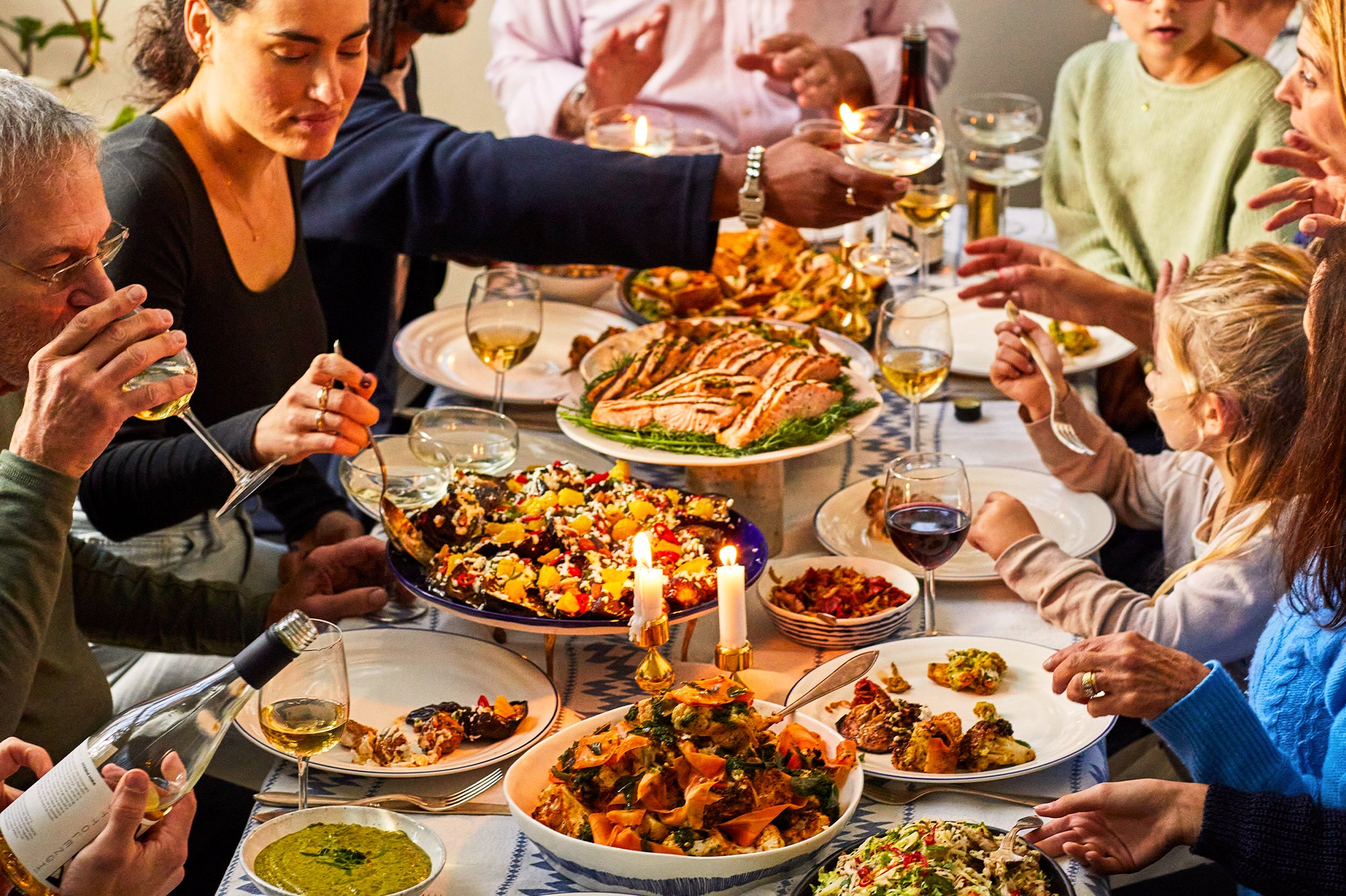 A dinner table with salad and salmon platters with people eating the meal. 