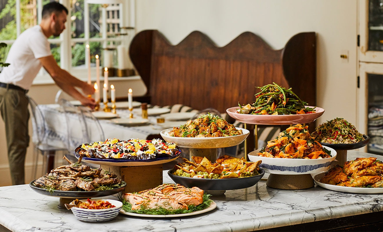 A display of salads with a man setting up a dinner table at the background